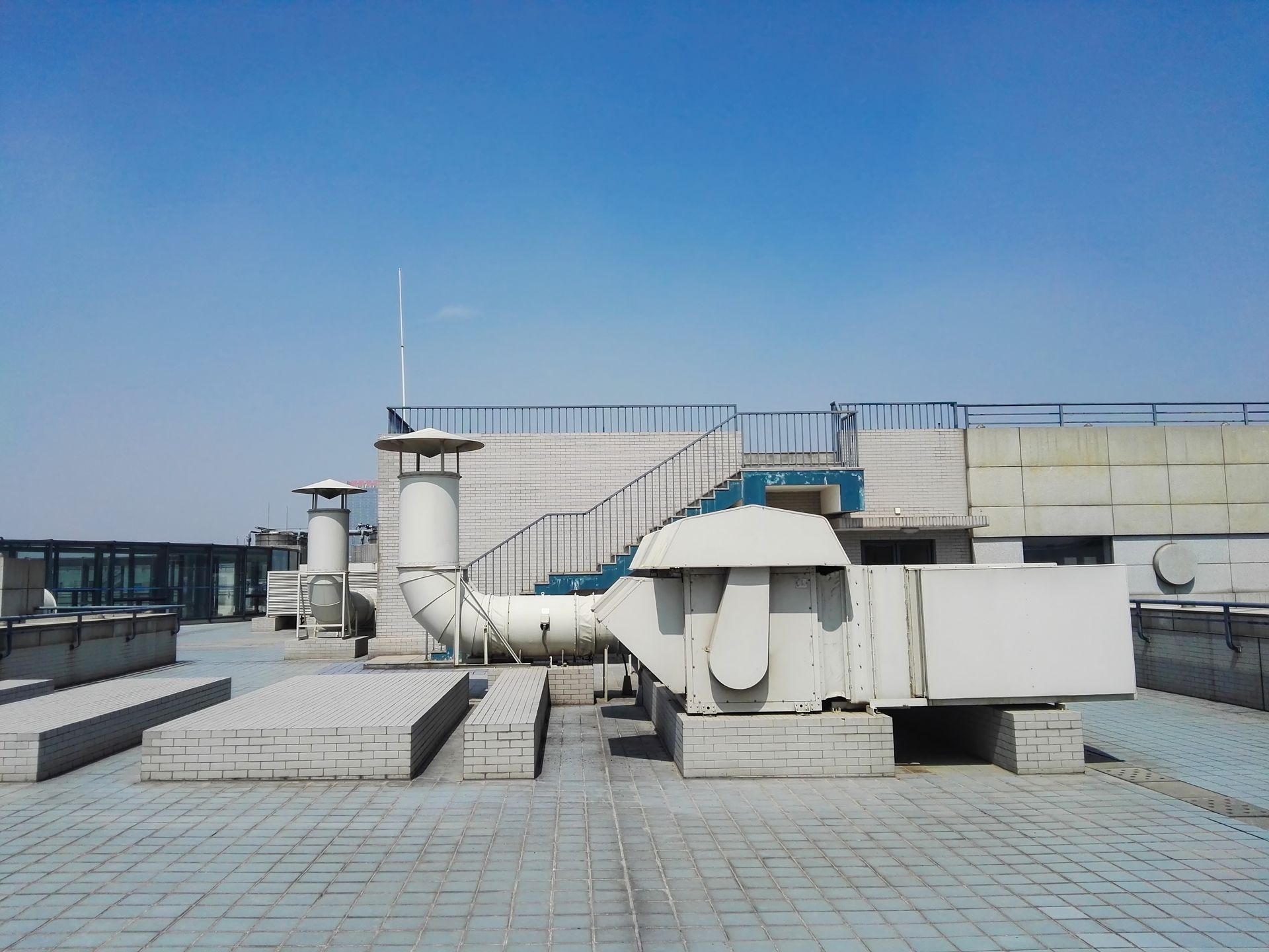 Rooftop with ventilation systems, stairs, and a clear blue sky.