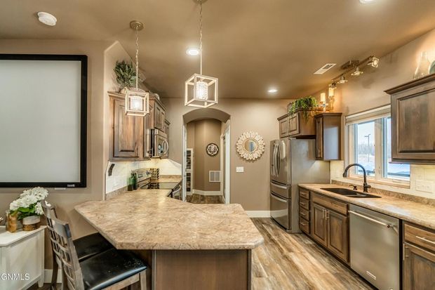 A modern kitchen featuring brown wooden cabinets, a granite island with bar stools, stainless steel appliances, and a window.