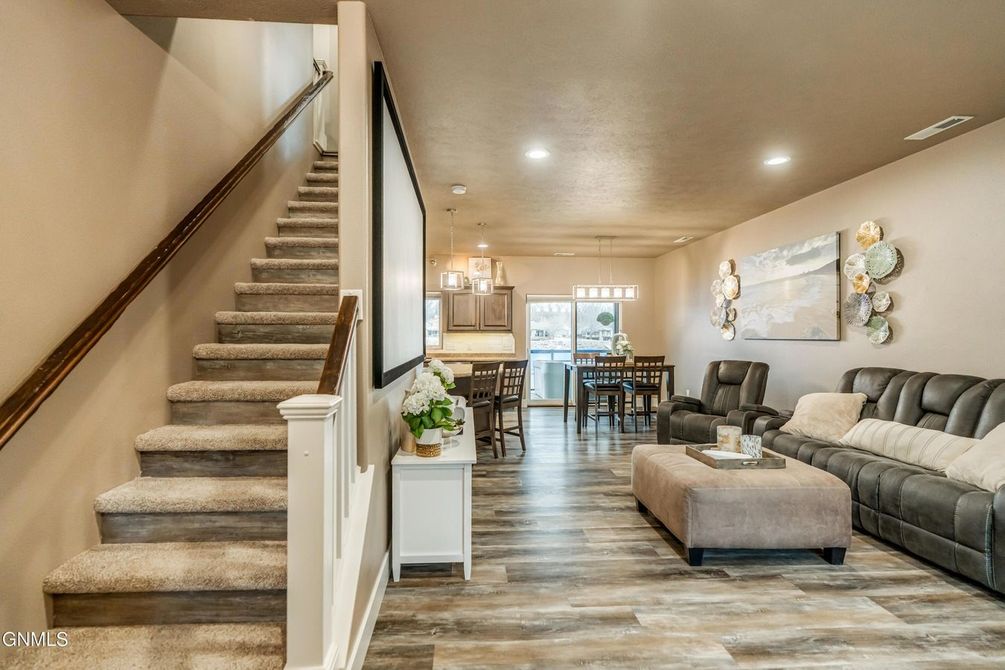 A wide-angle view of a modern open-concept living area with a carpeted staircase, gray sofa, dining table, and light floors.