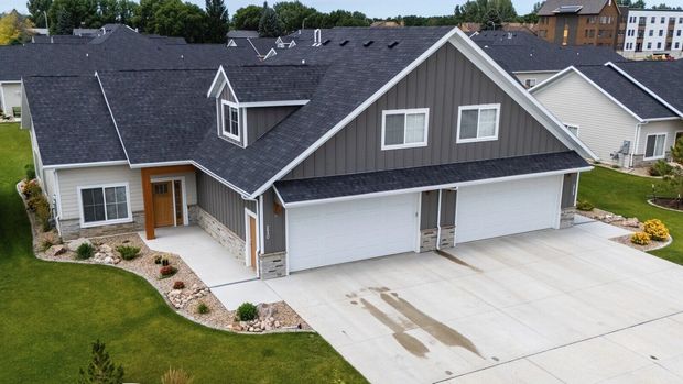 An aerial view of a multi-unit suburban house with dark gray roofing, wood-look siding, stone accents, and a concrete drive.