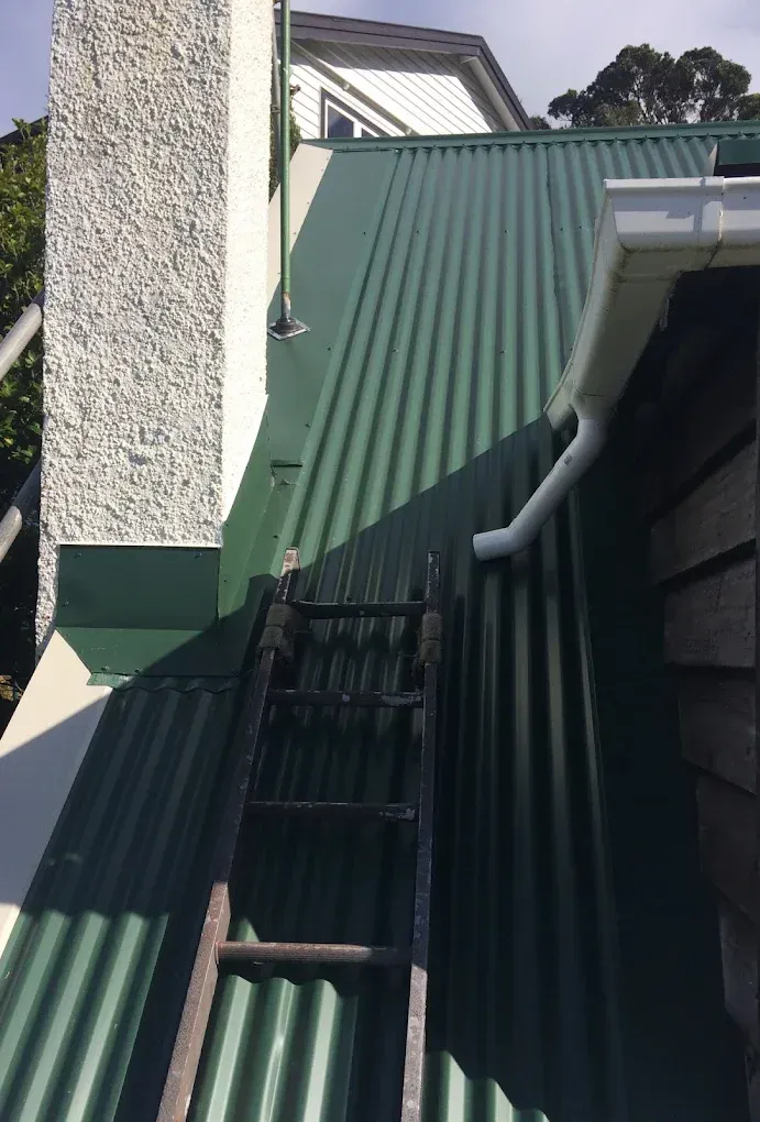 A man in a hat is standing on a gutter on the side of a building.