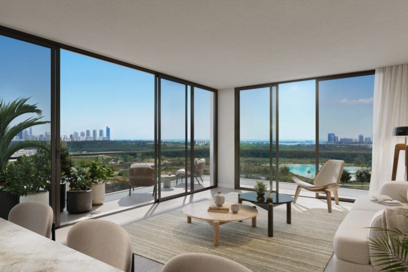 Modern living room with floor-to-ceiling windows overlooking a landscape. Furnished with neutral tones, plants and a view.