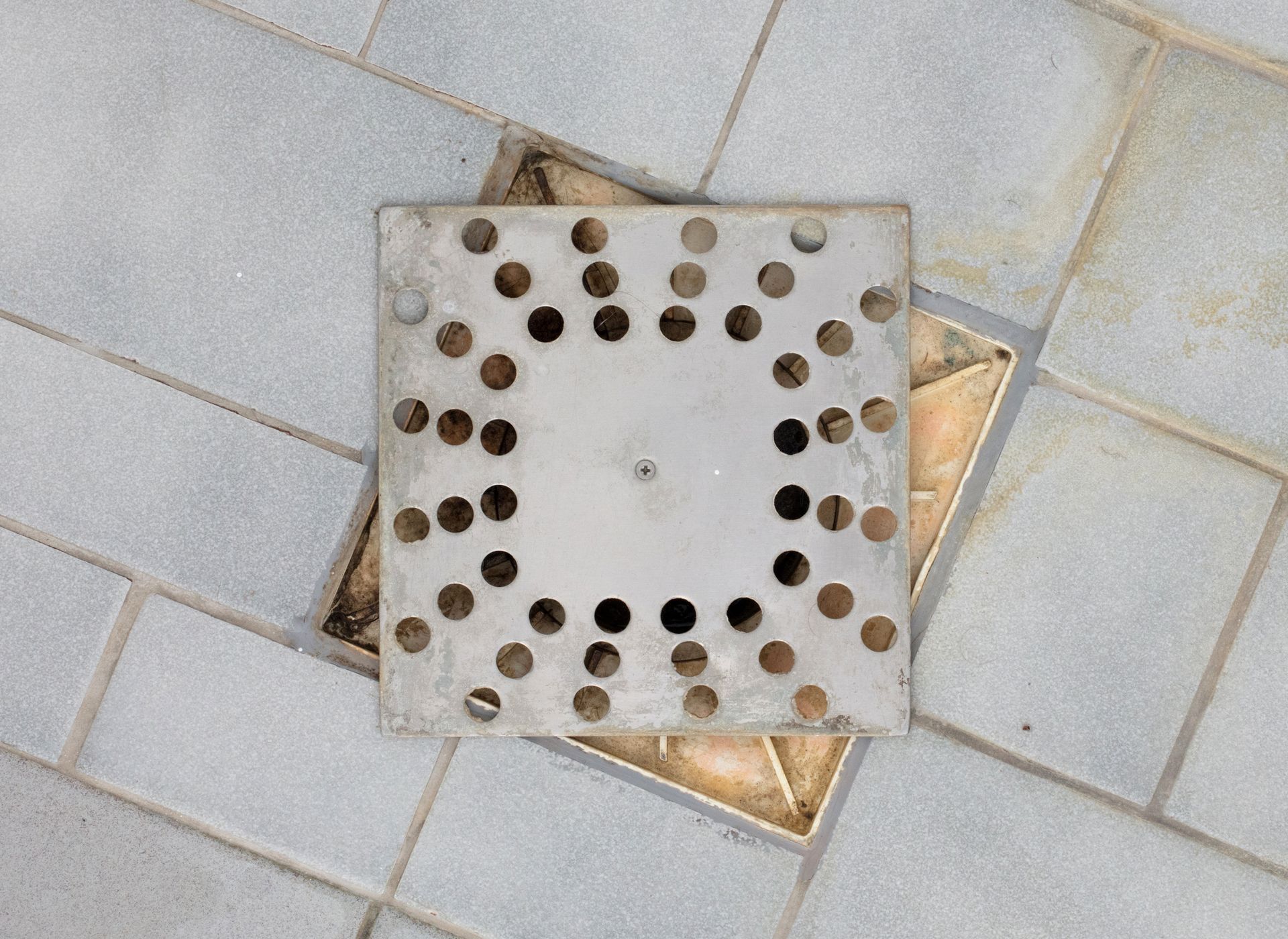 A square drain cover is sitting on a tiled floor.