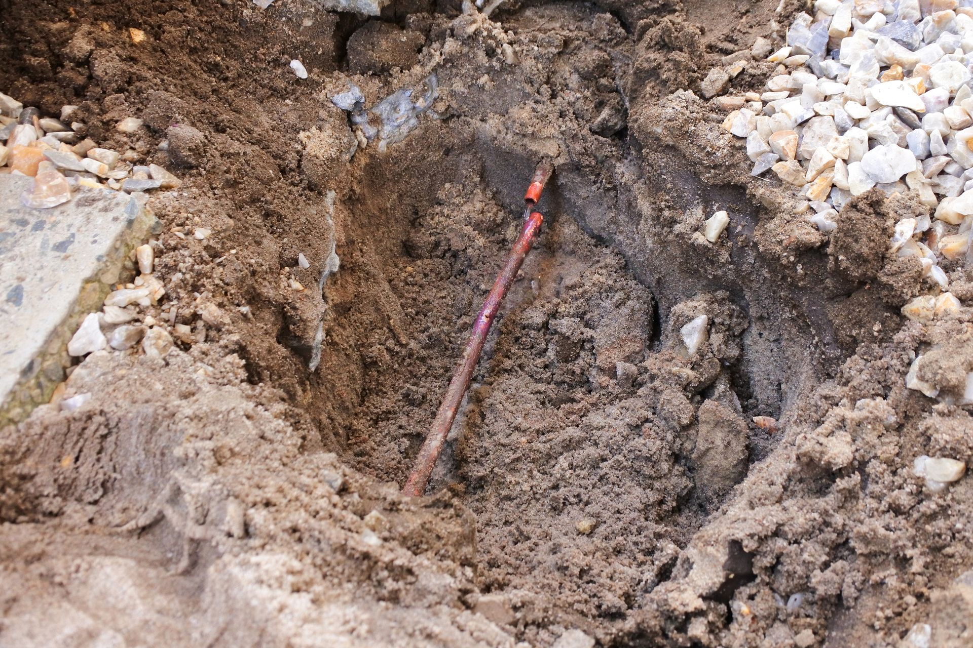 A red wire is sticking out of a hole in the ground.