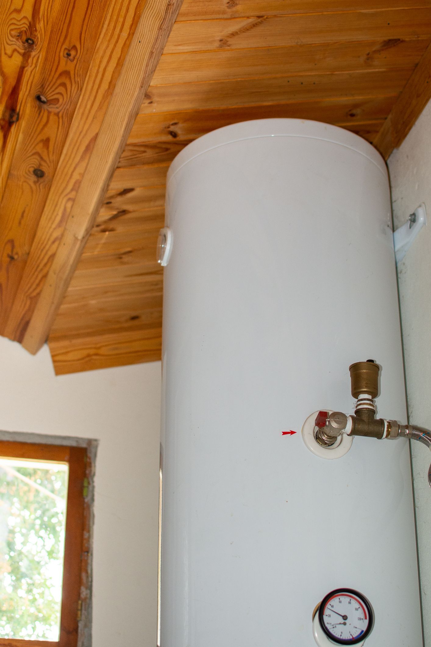 A white water heater is sitting in a room under a wooden ceiling.