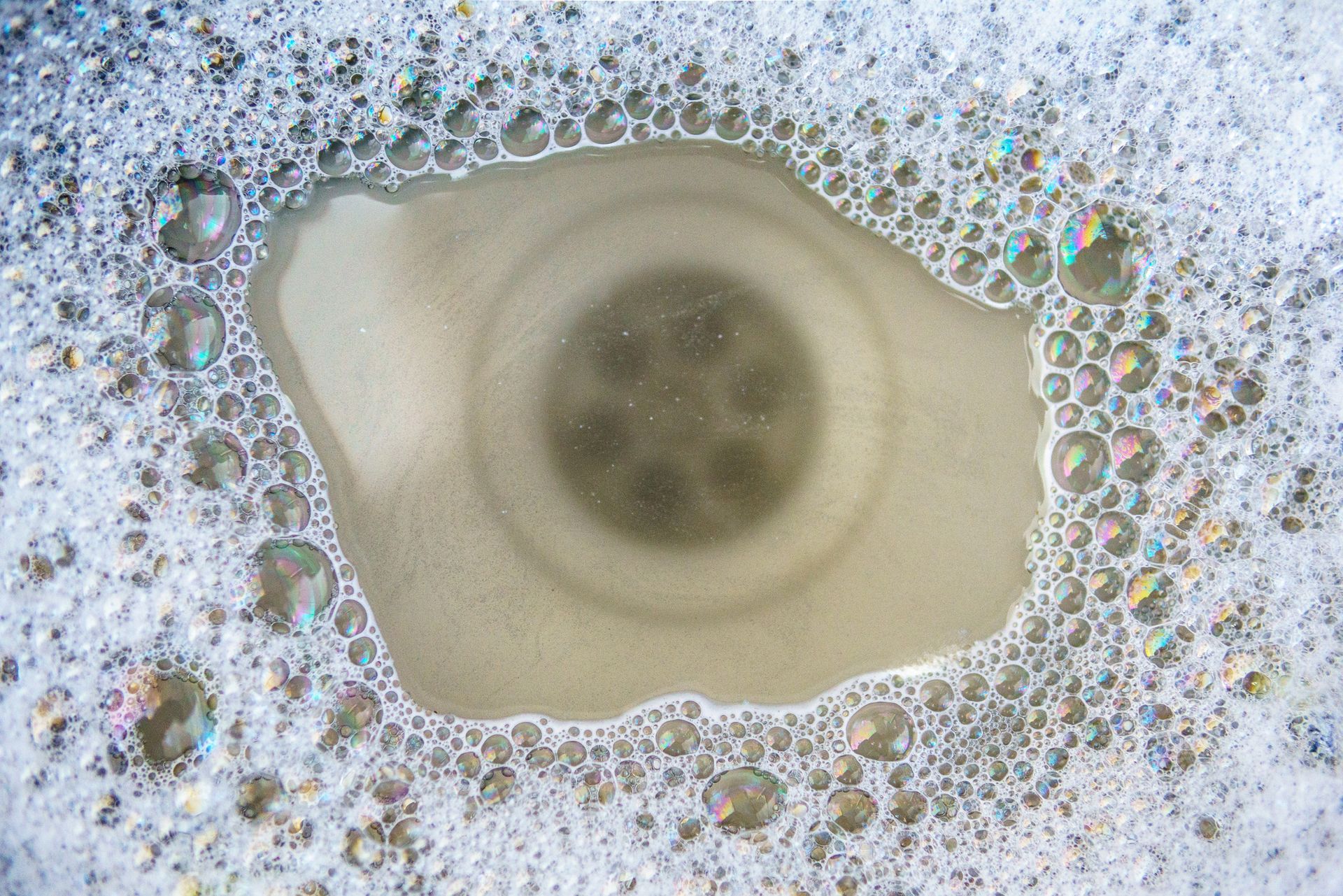 A sink drain filled with soapy water and bubbles.