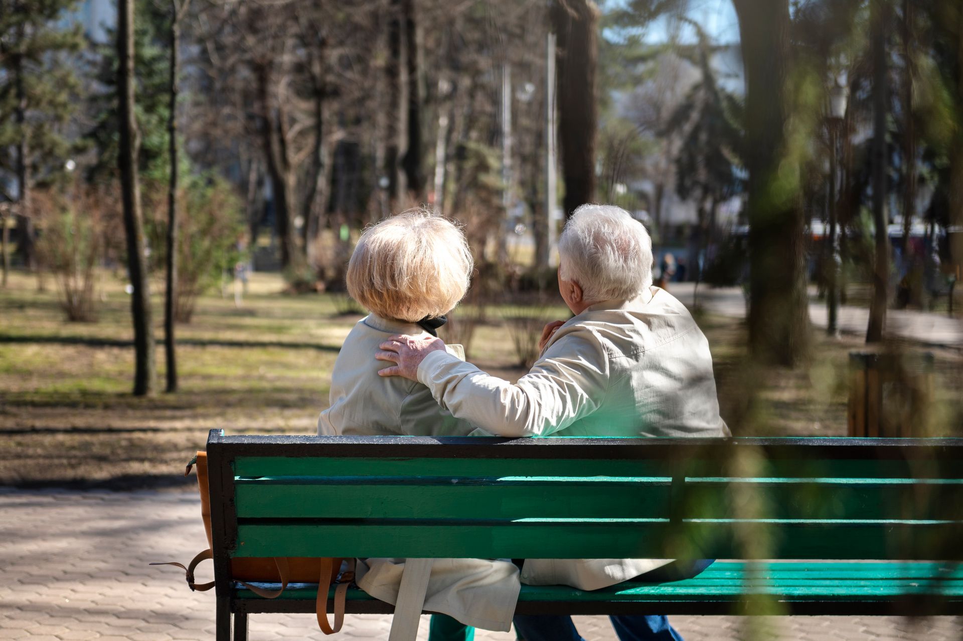 An elderly couple is sitting on a park bench.