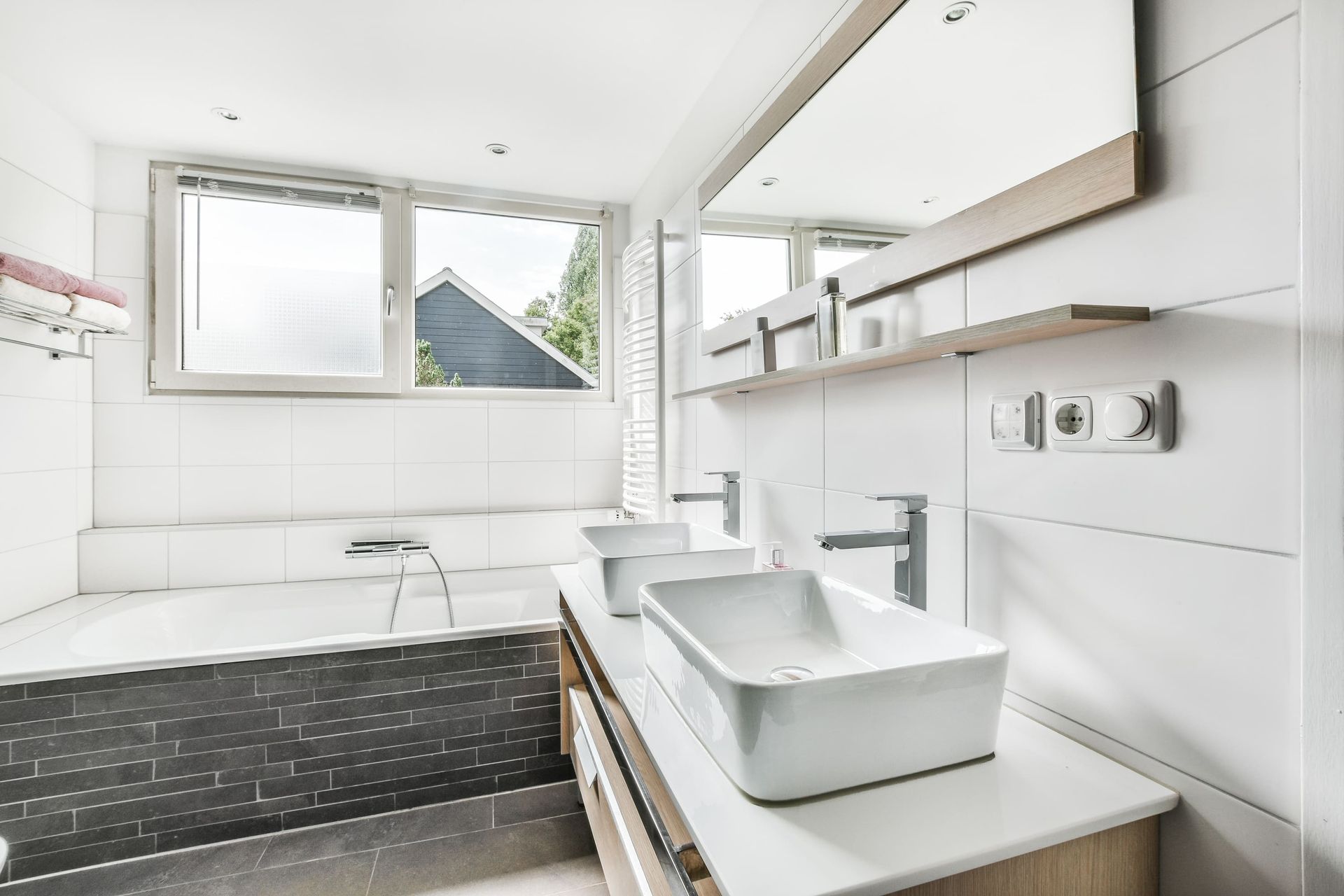 Modern bathroom with dark wood paneling, dual sinks, large mirror, and glass shower.