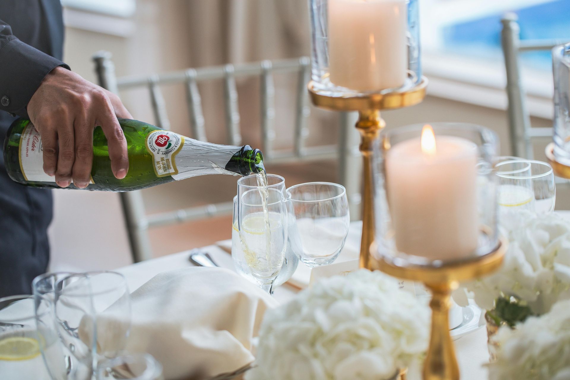 Person pouring champagne into glasses at a decorated table with candles and flowers.