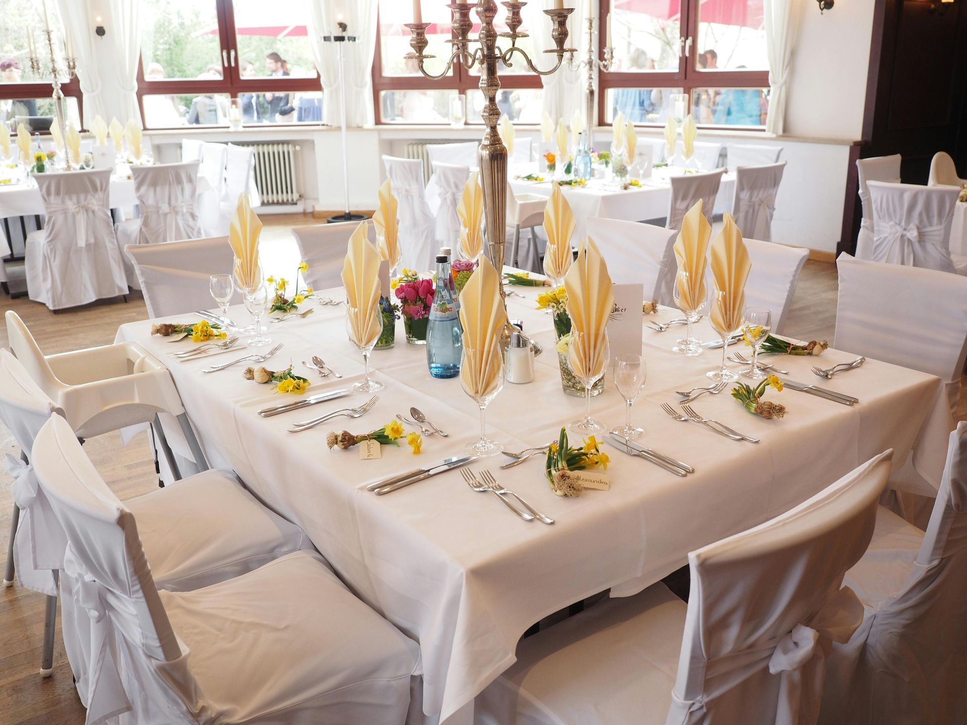 Elegant dining tables set for a celebration, white tablecloths, chairs with covers, floral centerpieces.