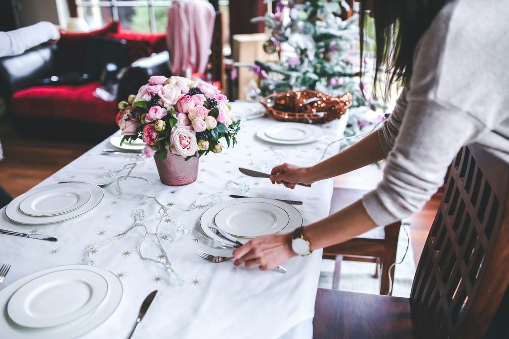 Person setting a formal dining table with pink flowers.