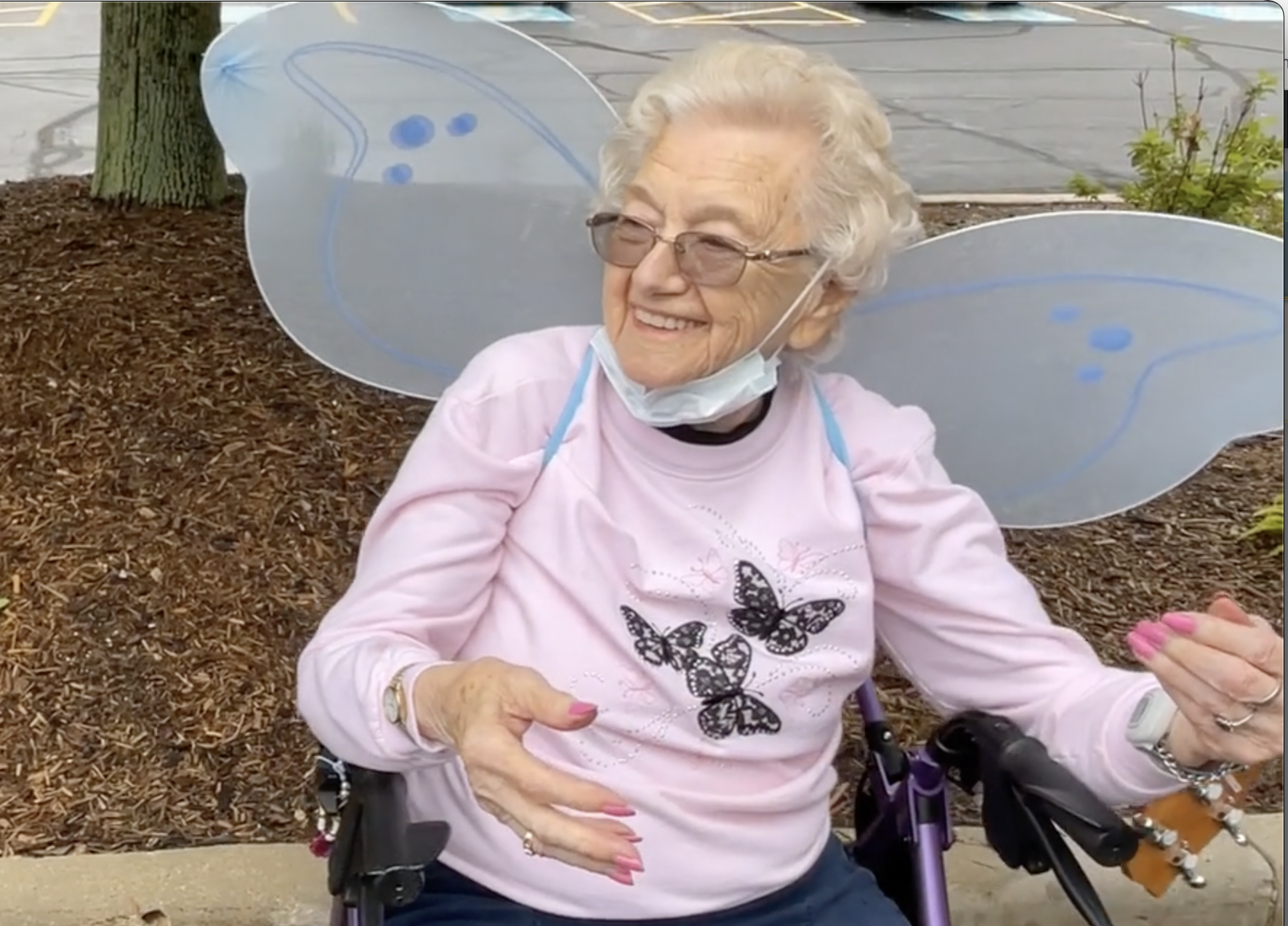 elderly woman in a pink butterfly shirt and wings release a butterfly