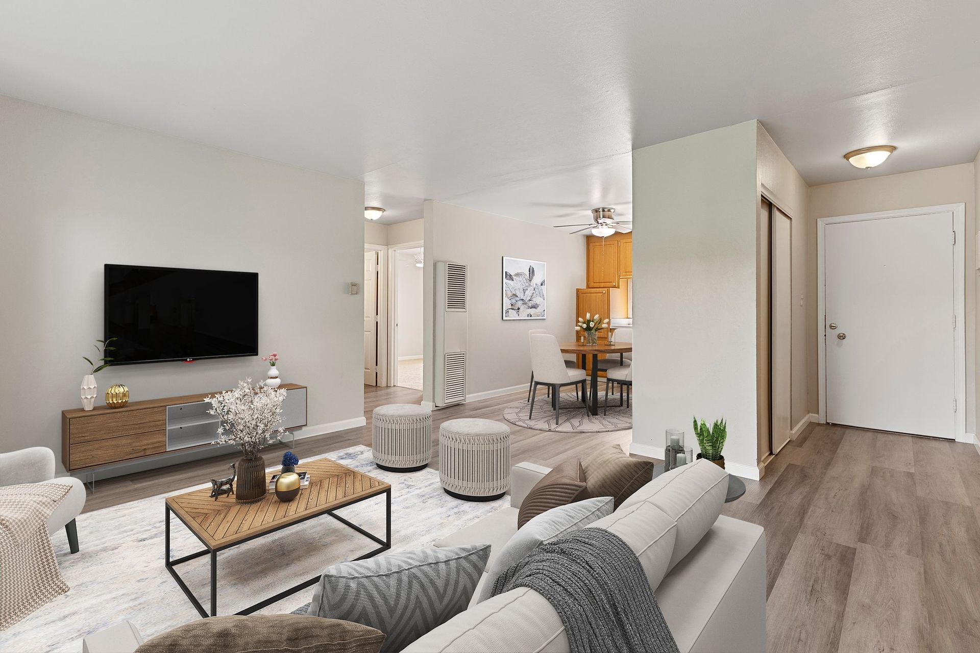A well-lit, modern open-concept living room featuring a gray sofa, TV on a wooden console, and a dining area in the back at Whispering Oaks in Concord, CA.