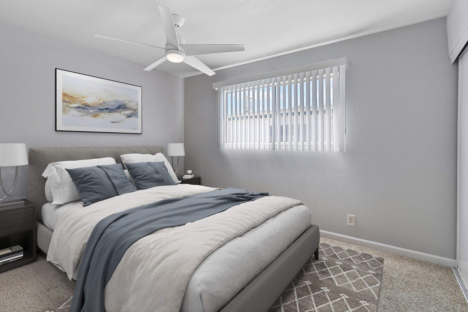 A modern bedroom featuring a bed with gray bedding, a white ceiling fan, and framed art on a light gray wall at Whispering Oaks in Concord, CA.