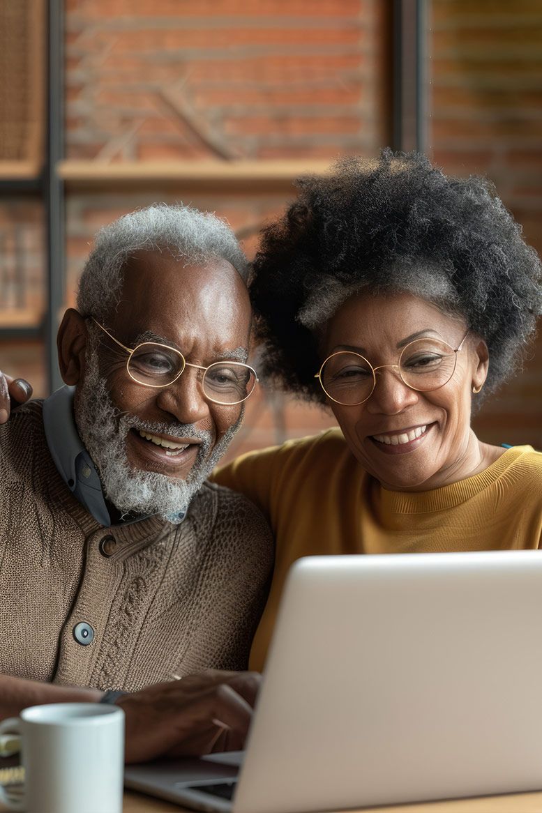 Older couple smiling while looking at a laptop computer. One person has an arm around the other.