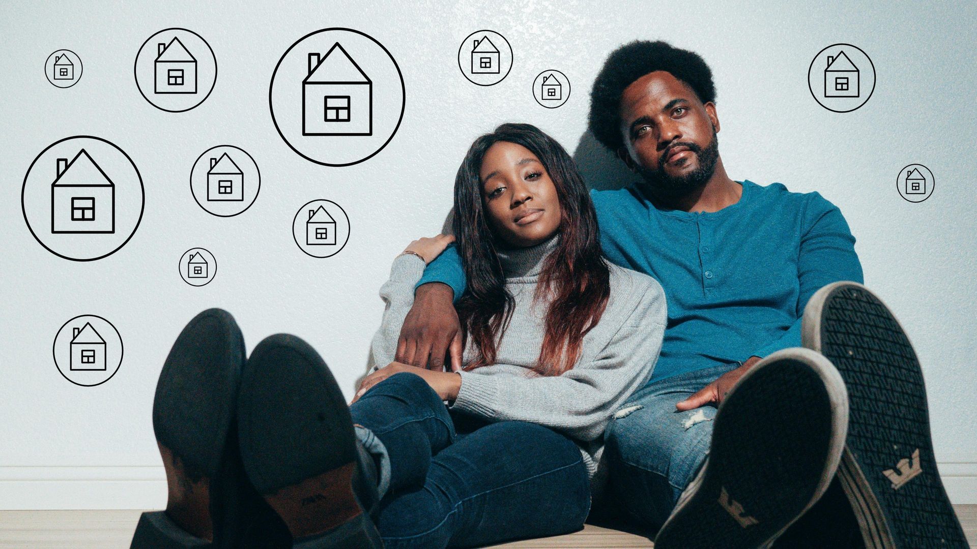 Couple sitting on the floor in front of a wall with house icons, looking thoughtful about home buying