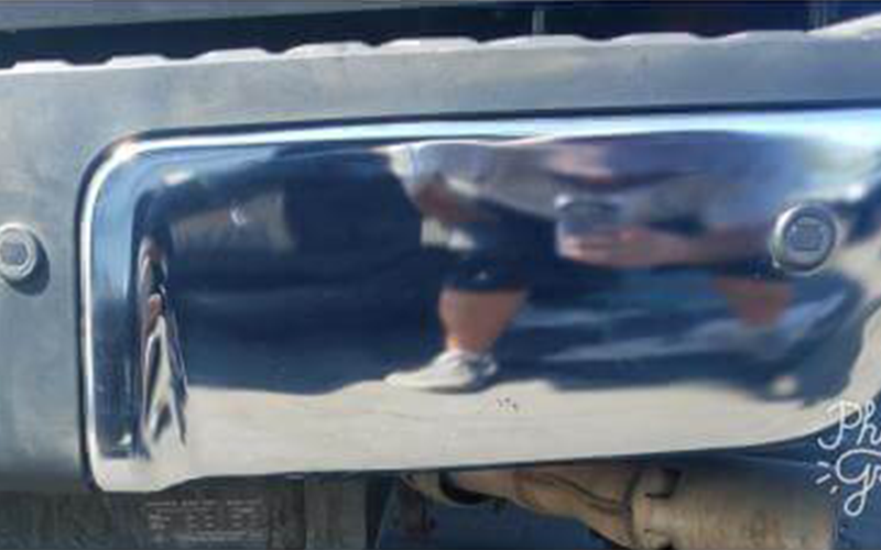 Chrome bumper reflecting a person holding a phone, on a gray truck.