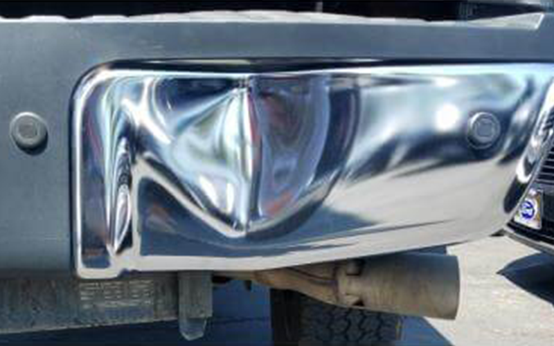 Chrome truck bumper with a dent, exhaust pipe visible.