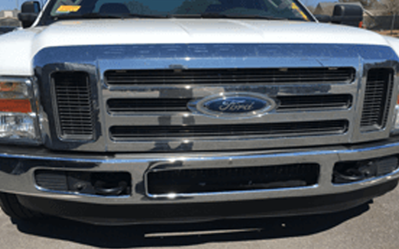 Close-up of a white Ford truck's front end, with a chrome grill, bumper, and Ford logo.