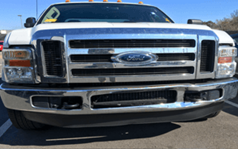 White Ford truck, front view, chrome grill and bumper, parked outside on a sunny day.