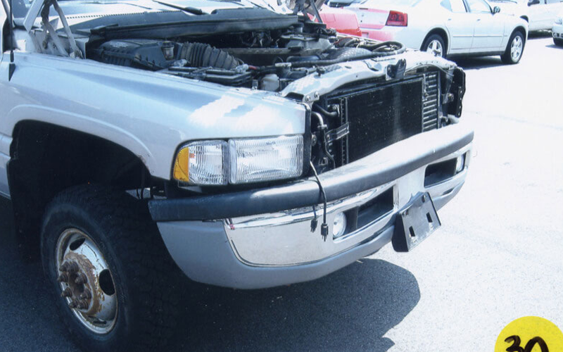 Damaged silver Dodge Ram truck, hood open, with missing front grille and license plate holder.