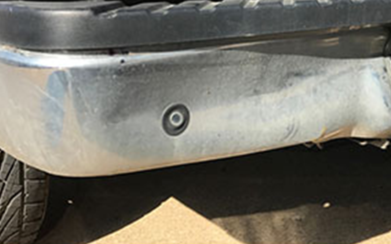 Close-up of a silver truck bumper with a black sensor and dirty surface.