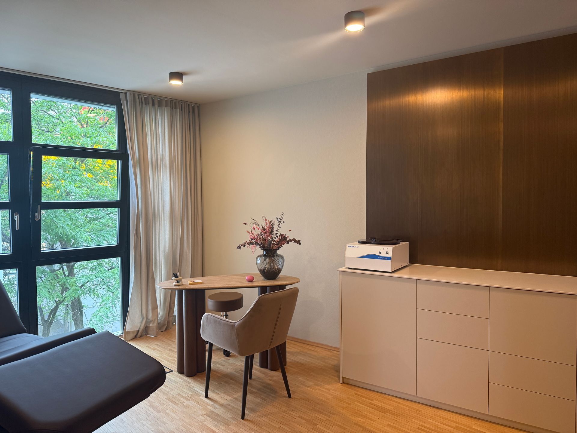 Ein Wohnzimmer mit einem Tisch, Stühlen, einer Vase mit Blumen und einem Gemälde an der Wand. Muskelrelaxans