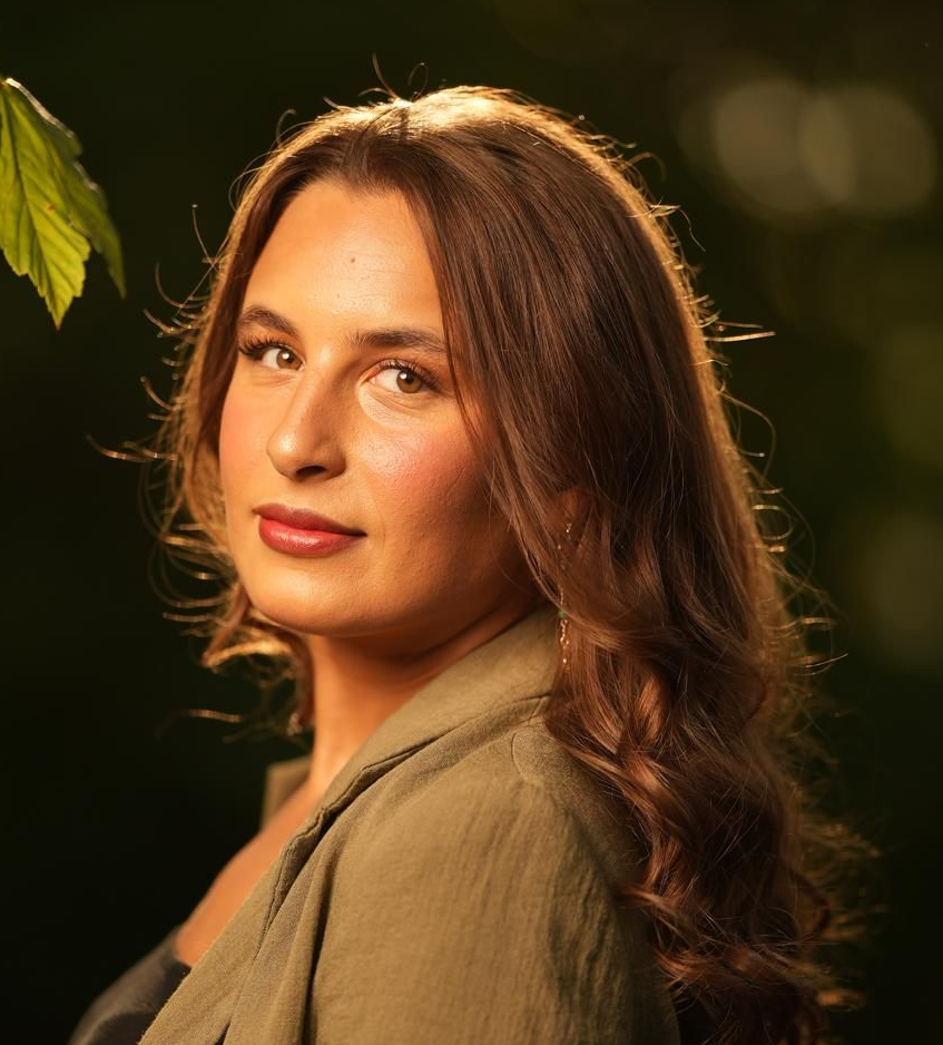 Eine Frau in einer grünen Jacke steht vor einem Baum.