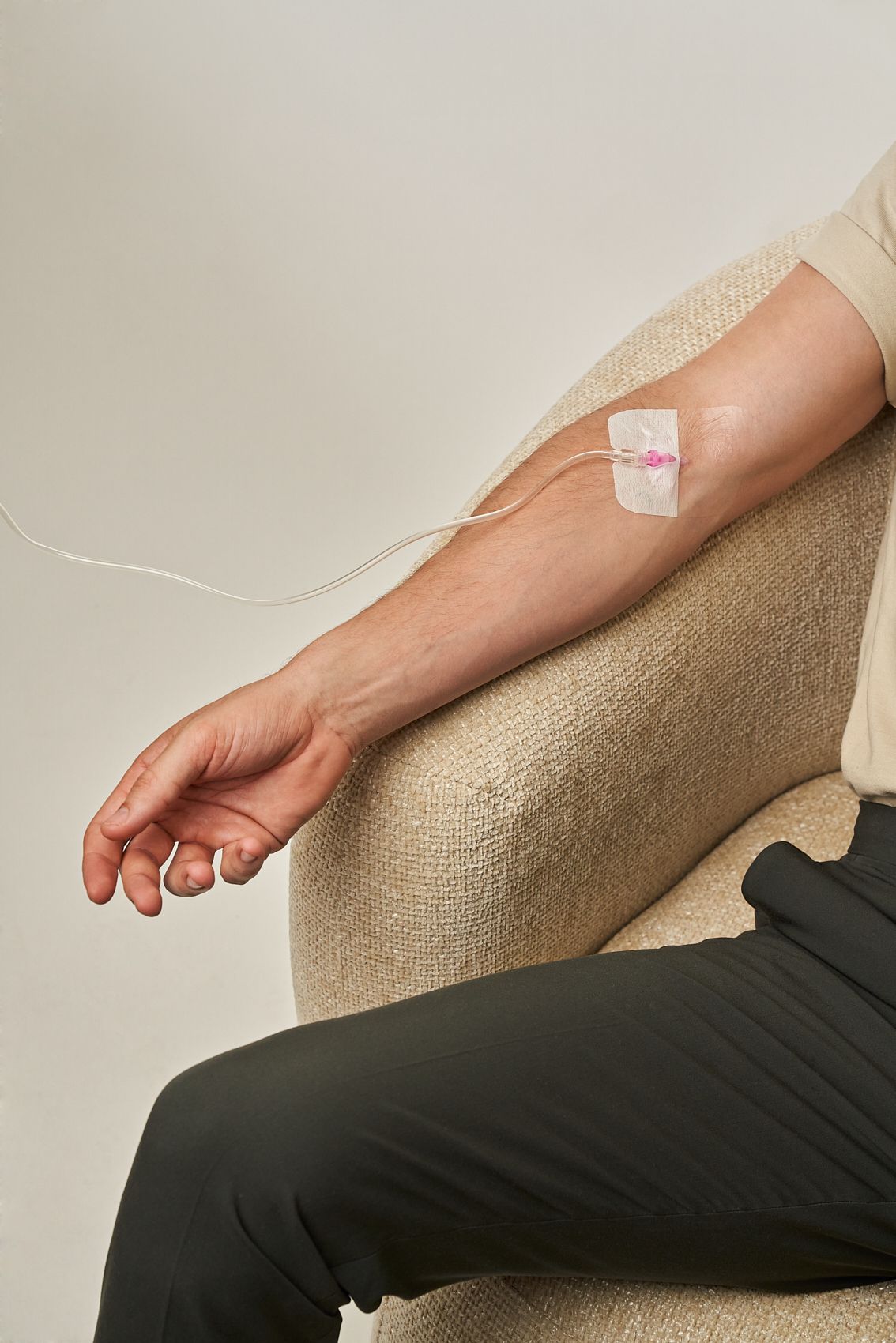 Ein Mann sitzt auf einem Stuhl mit einer Infusion im Arm. Preise  NAD+ Infusion gegen chronische Müdigkeit. 
