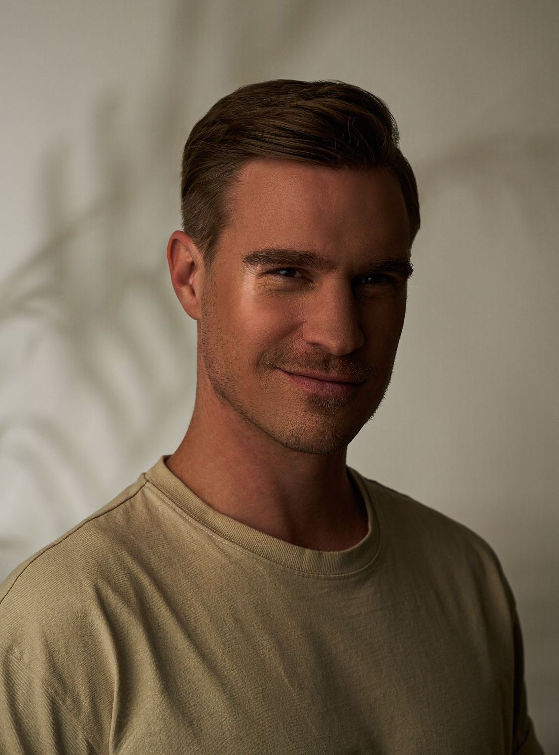 Ein Mann in einem beigen Hemd lächelt im warmen Licht.