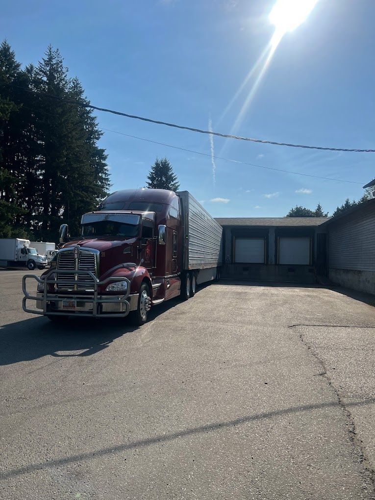 A red semi truck is parked in a parking lot next to a building.