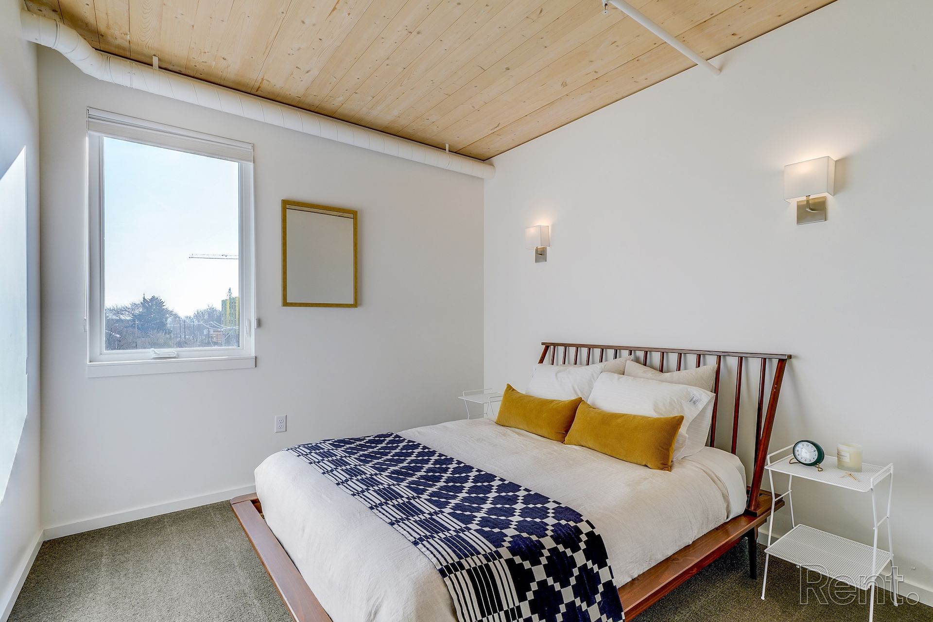 Bedroom with bed, pillows, blanket, window, and wood ceiling.