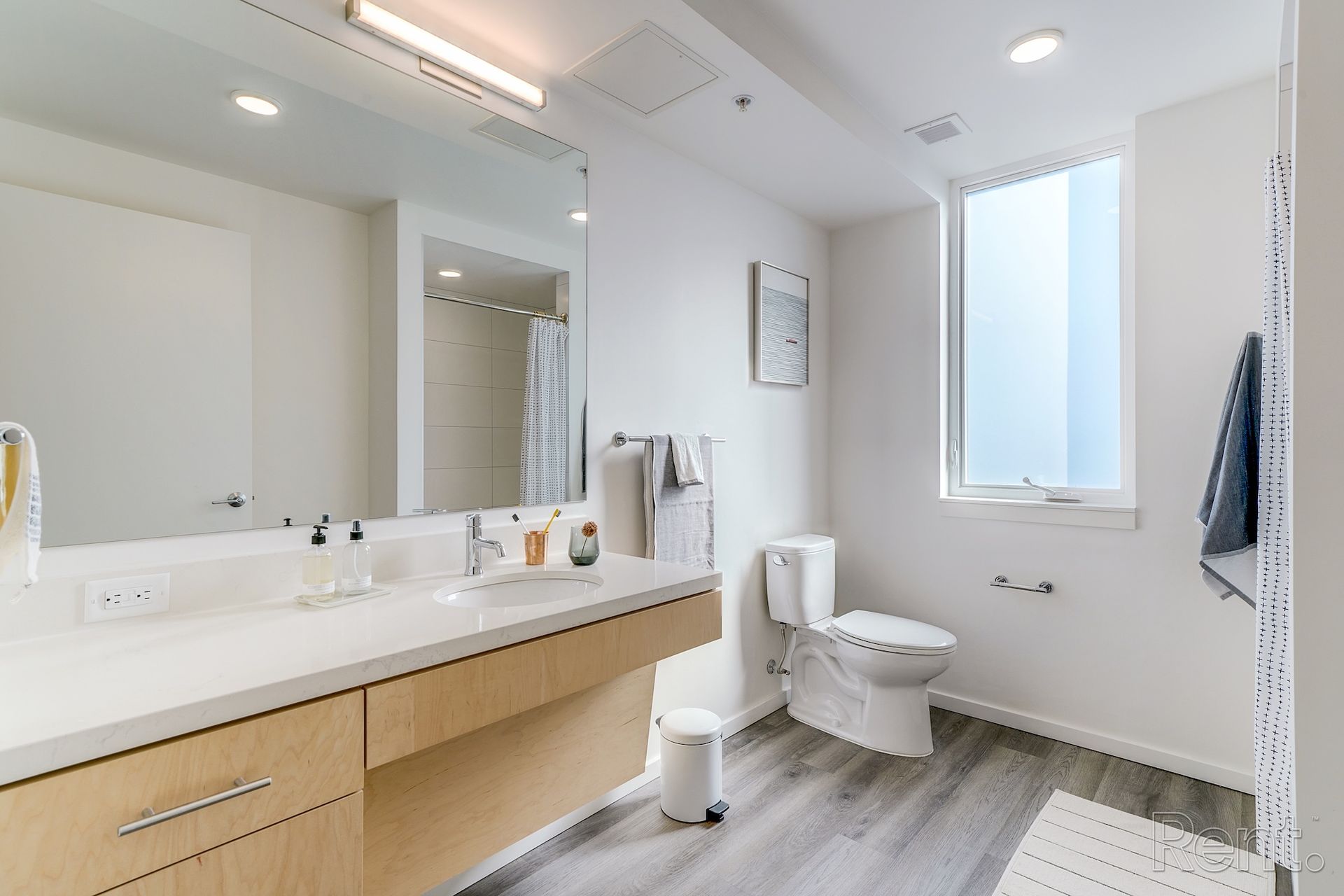 Modern bathroom with white walls, light wood vanity, large mirror, and gray flooring.