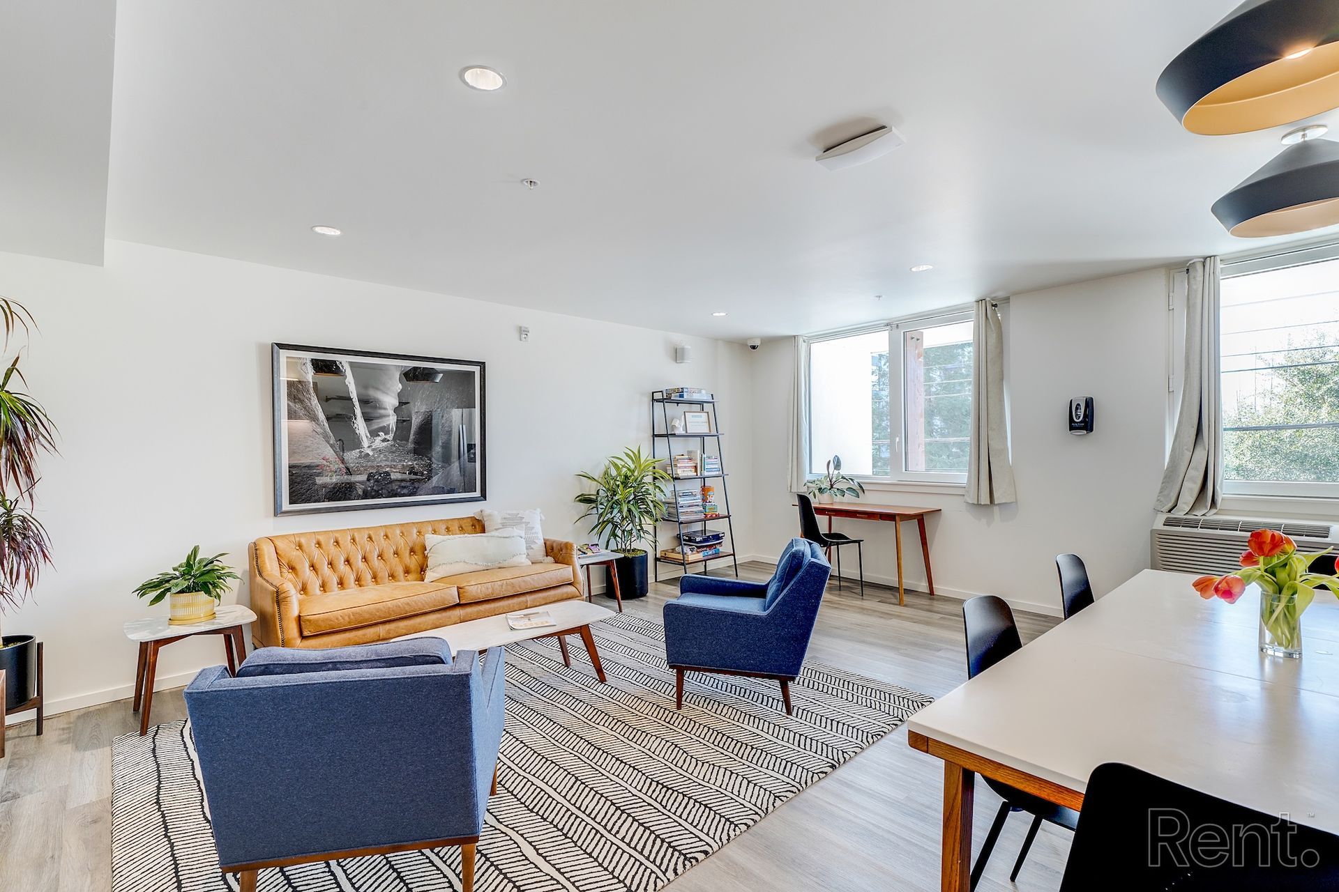 Spacious living room with tan tufted sofa, two blue armchairs, zebra rug, and dining table by a window.