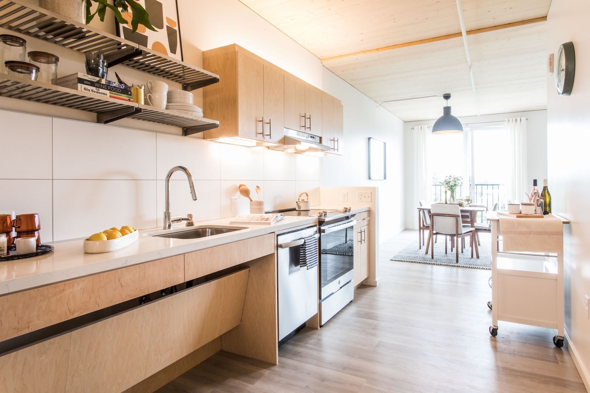 Modern kitchen with wood cabinets, white countertops, stainless steel appliances, and a dining area.