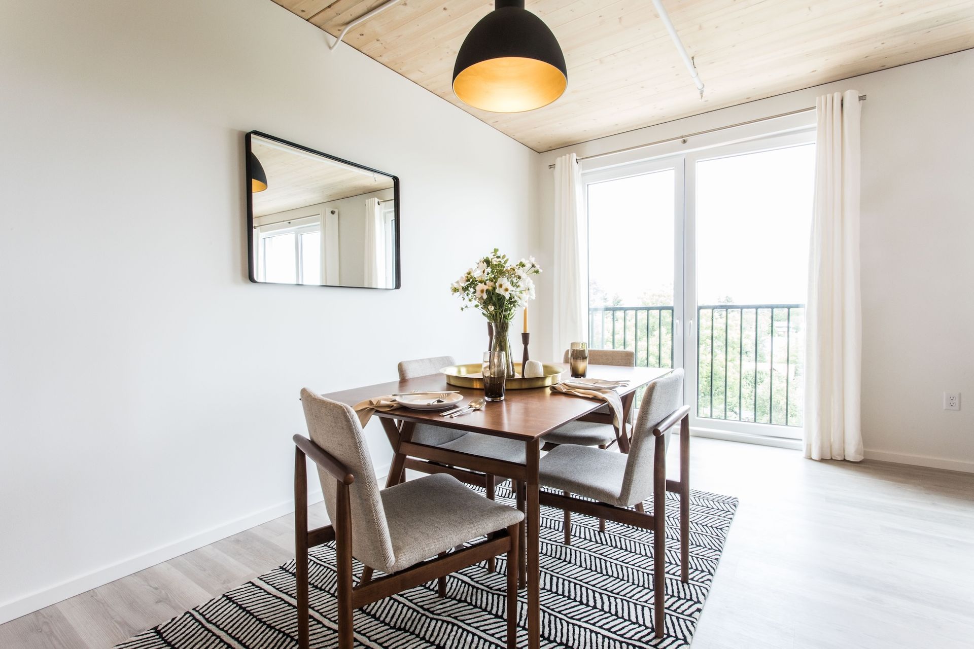Dining room with a wooden table, four chairs, a mirror, and a black and white rug.