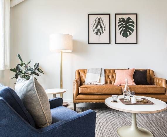 Living room with leather sofa, blue chair, floor lamp, round table, and botanical art.