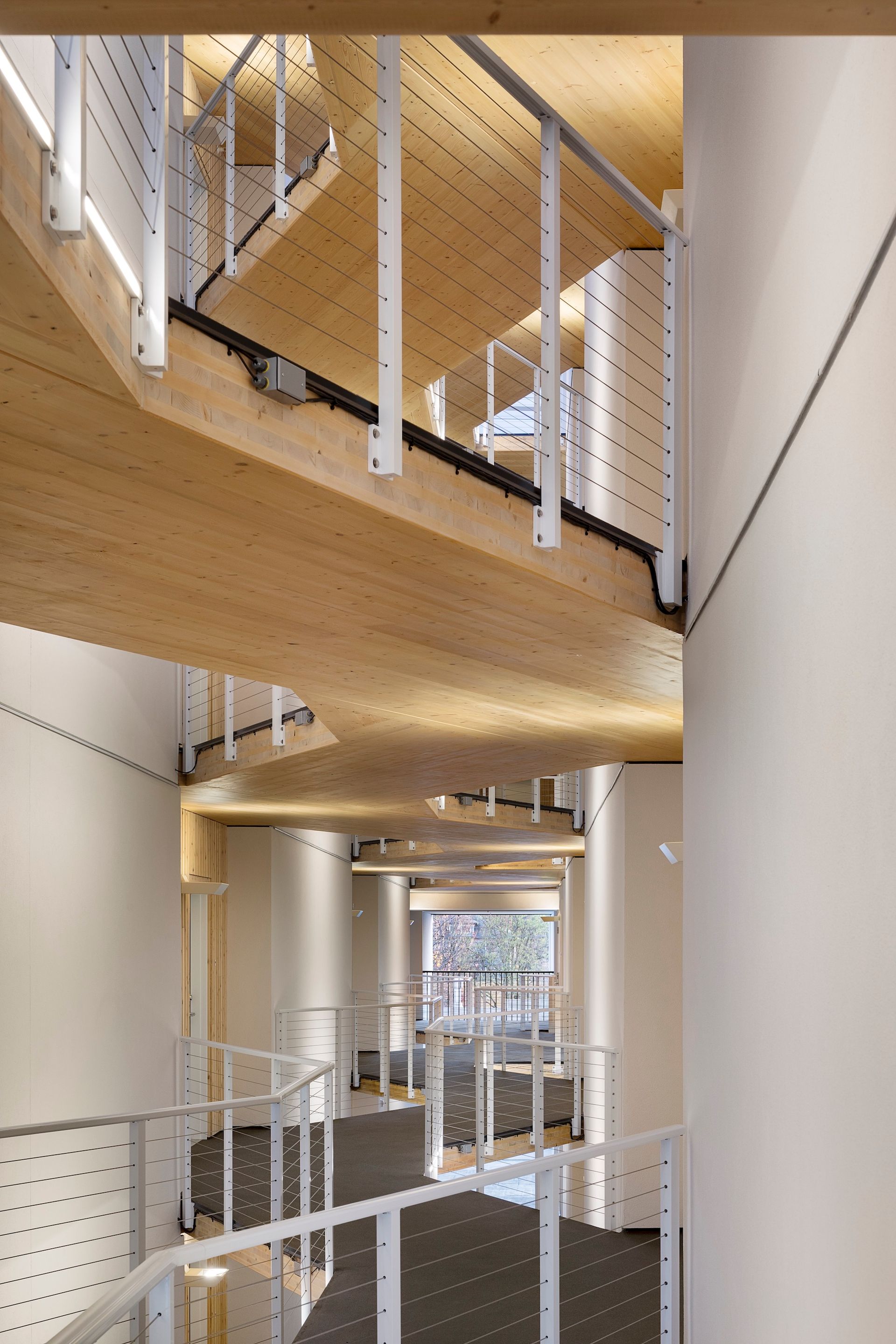 Wooden spiral staircase with white railing and support posts. Brightly lit interior.