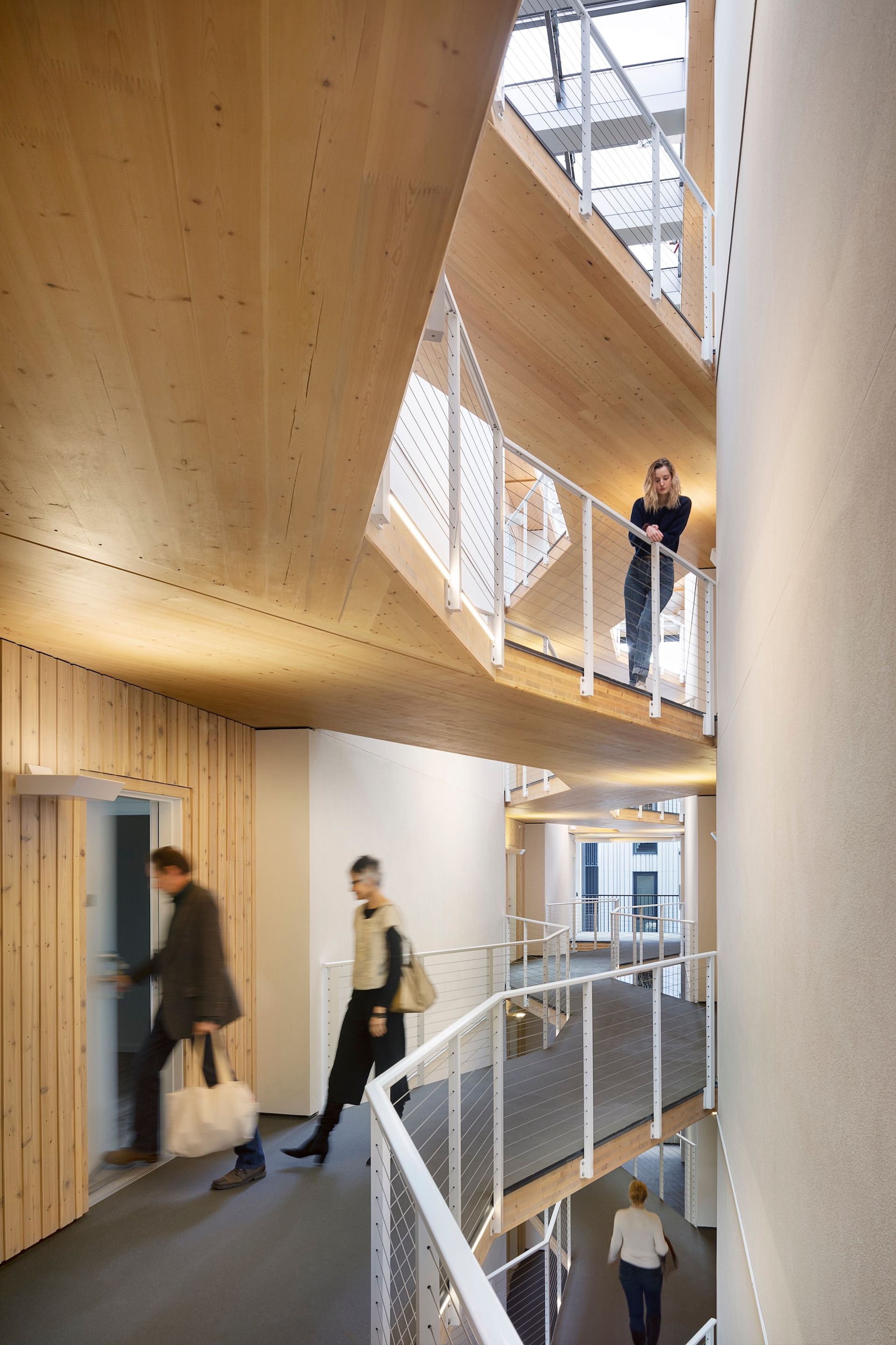 Interior view of wooden stairwell with people walking and standing. Natural light streams in.