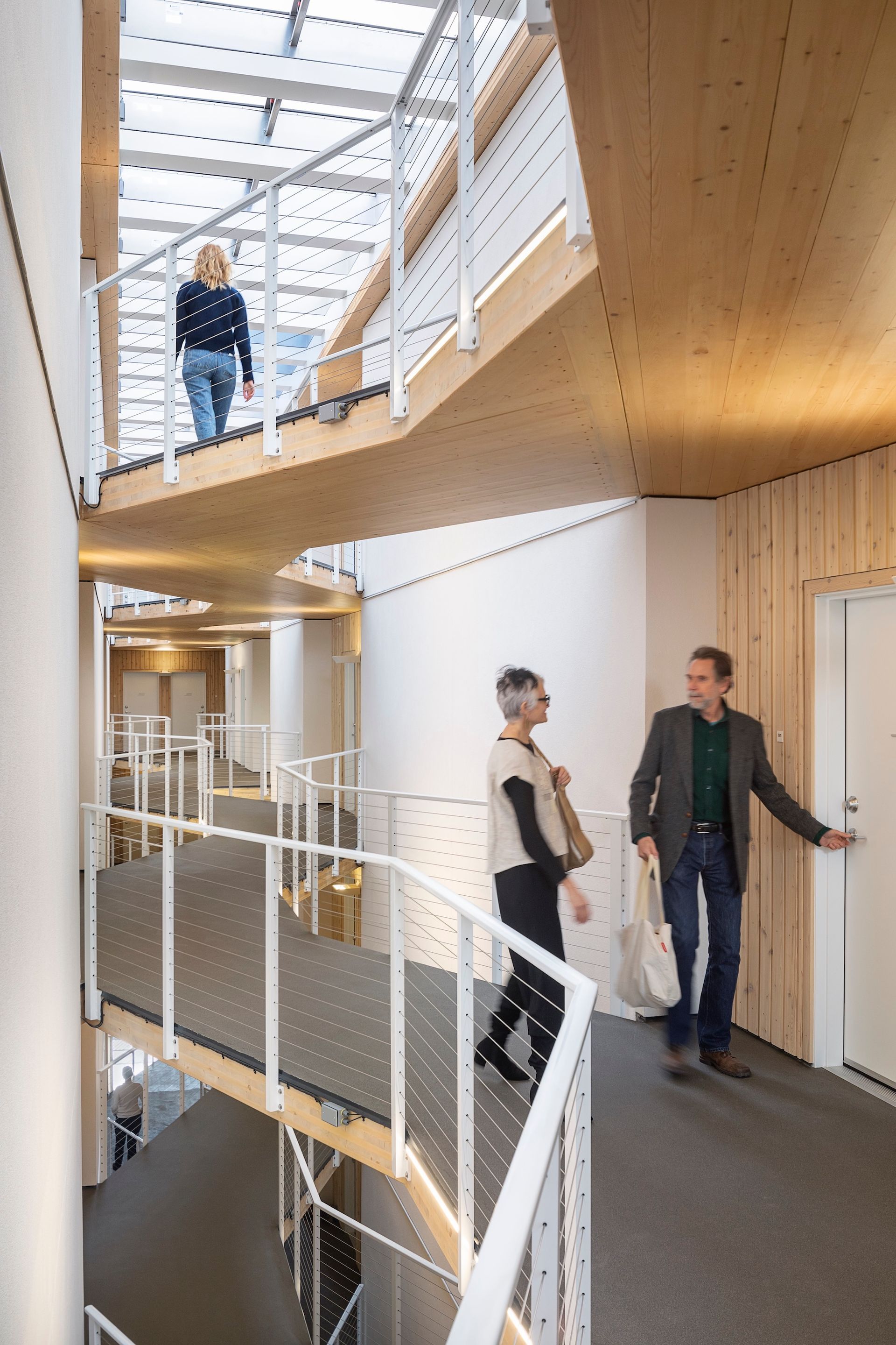 Interior with multi-level hallway, wood and white design, three people, stairs.