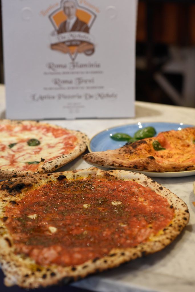 Pizze sul bancone: una con formaggio e basilico, un'altra con salsa e una terza con salsa di pomodoro. Sullo sfondo, una scatola bianca per pizza.