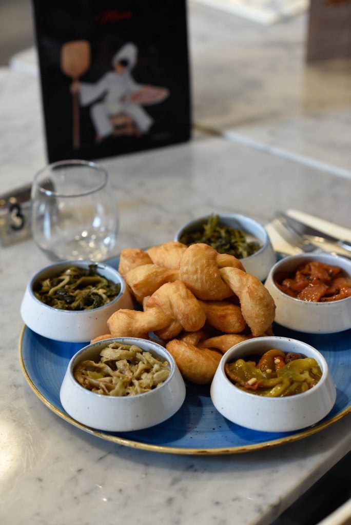 Piatto di antipasti con pasta fritta e piccole ciotole di condimenti vegetali colorati.