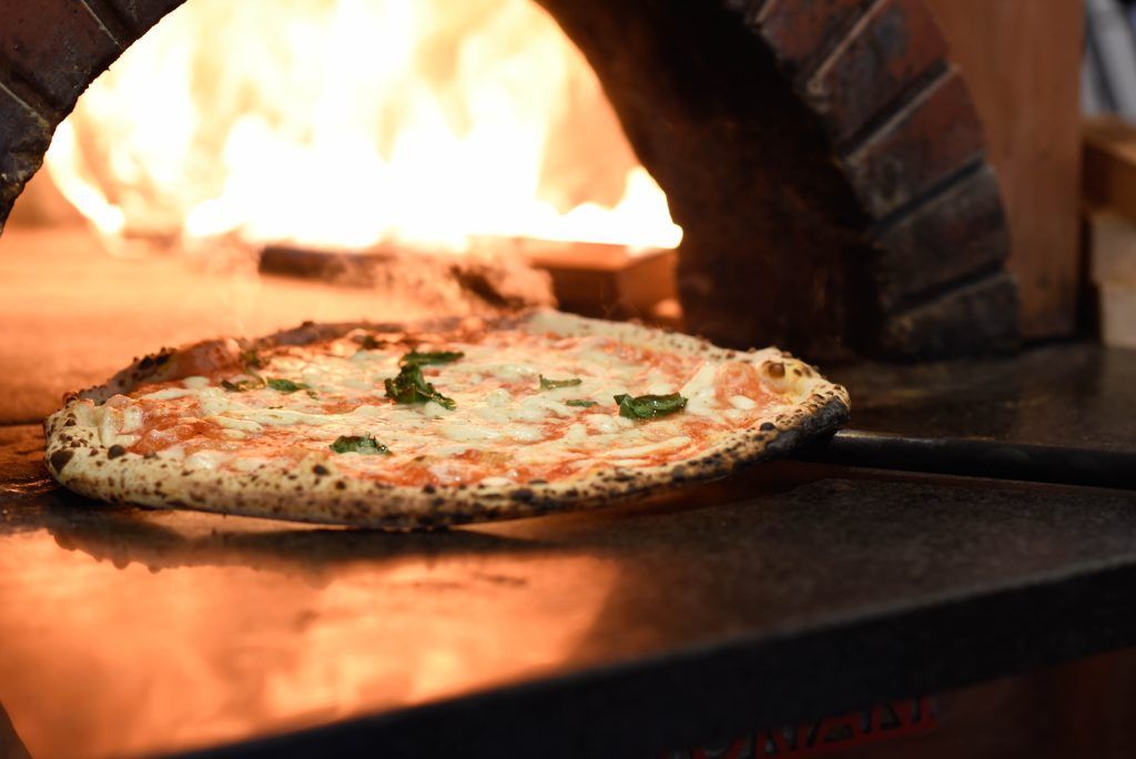 Pizza cotta in un forno a legna, fiamme visibili.