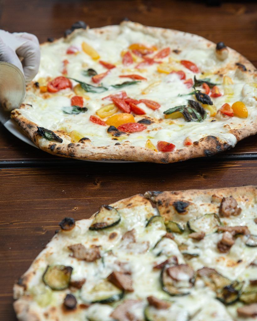 Due pizze su un tavolo di legno. Una con pomodori e basilico, l'altra con zucchine e altri condimenti.