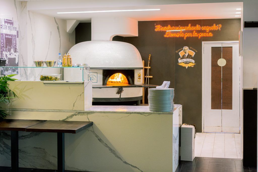 Forno per pizza in un ristorante, con bancone e zona pranzo visibili.