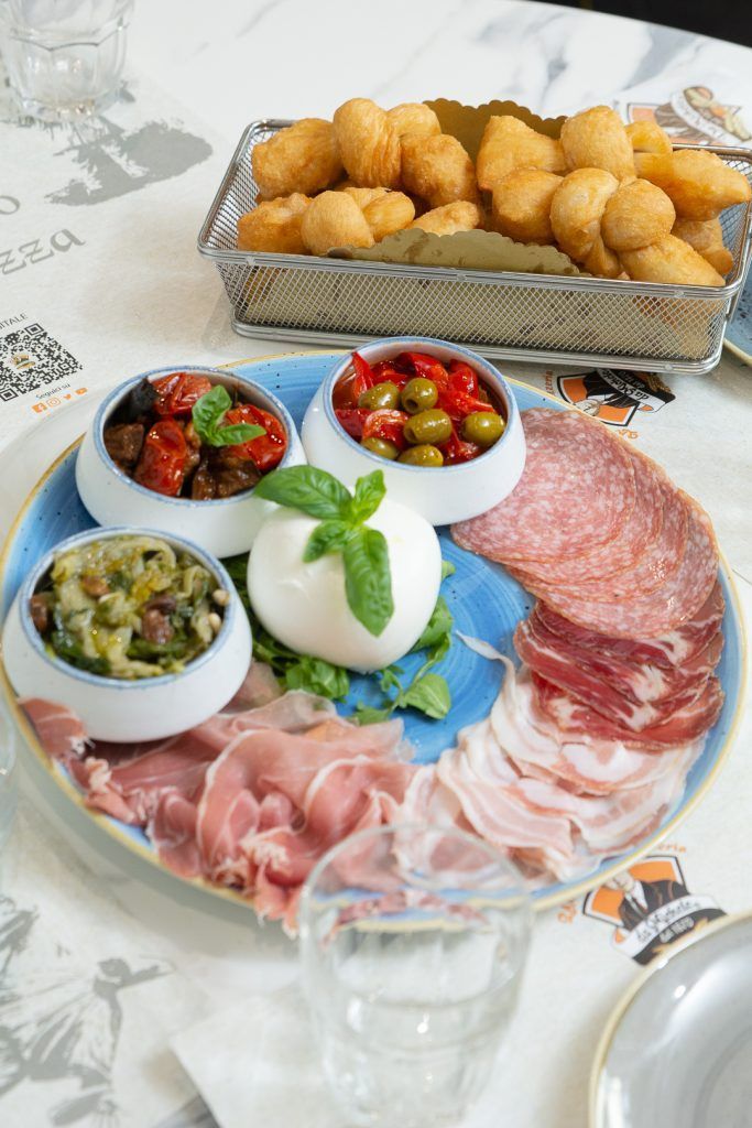 Piatto di antipasti con salumi italiani, formaggi e palline di pasta fritte su un tavolo.