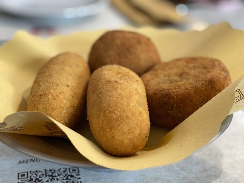 Cibo fritto in un cestino foderato di carta gialla. Include due pezzi cilindrici e due rotondi con crosta dorata.