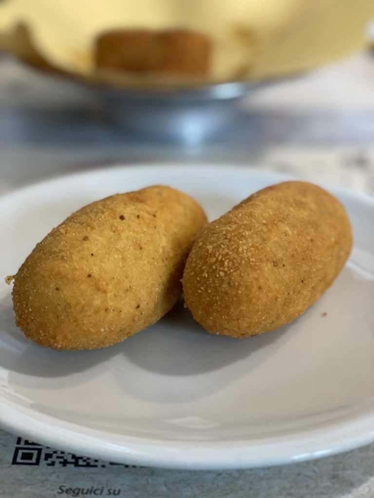 Due crocchette dorate e fritte su un piatto bianco; un'altra crocchetta sullo sfondo sfocato.