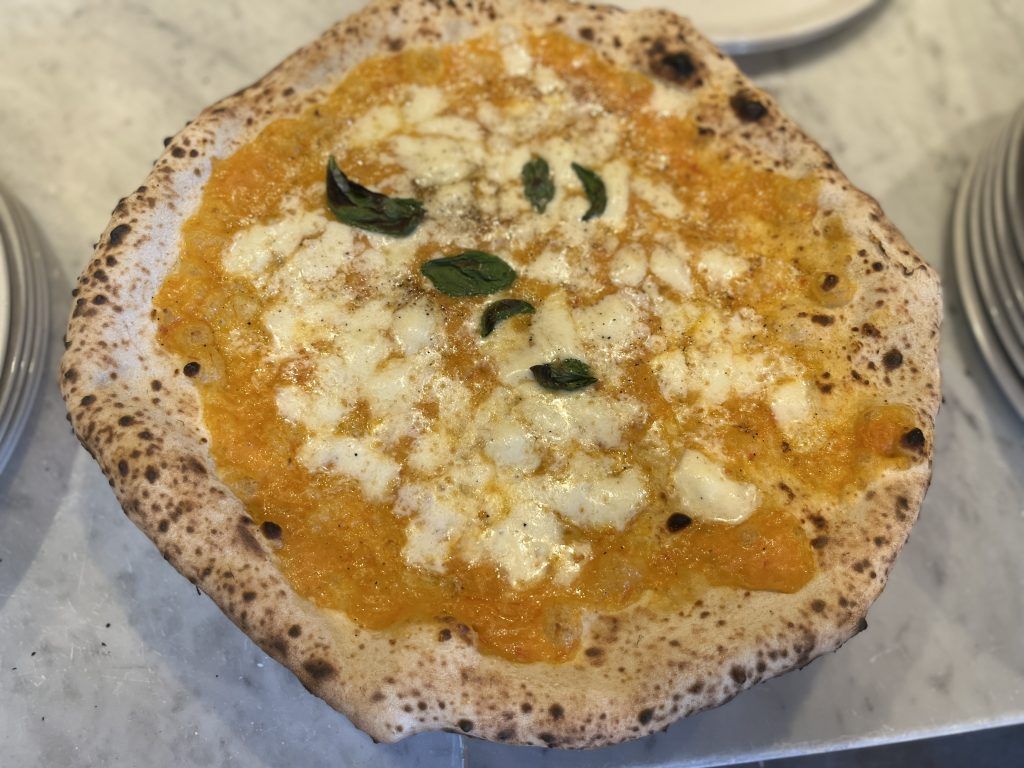 Pizza con salsa all'arancia e formaggio bianco, guarnita con basilico verde su una base rustica.