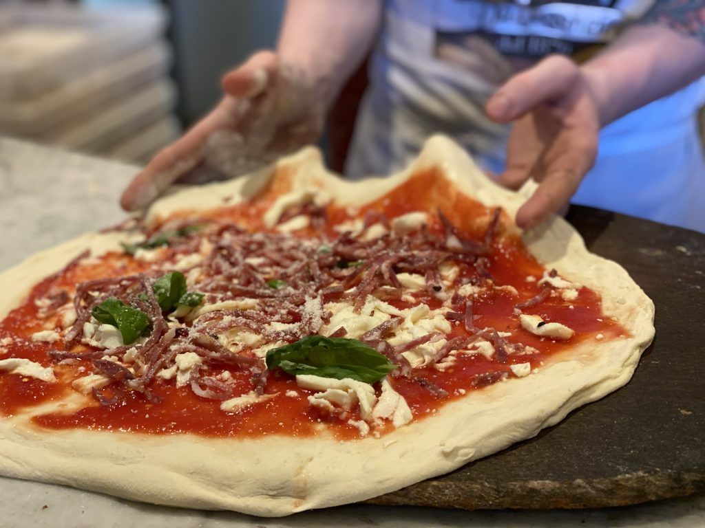 Preparazione della pizza: impasto con salsa, formaggio e carne maneggiati a mano.